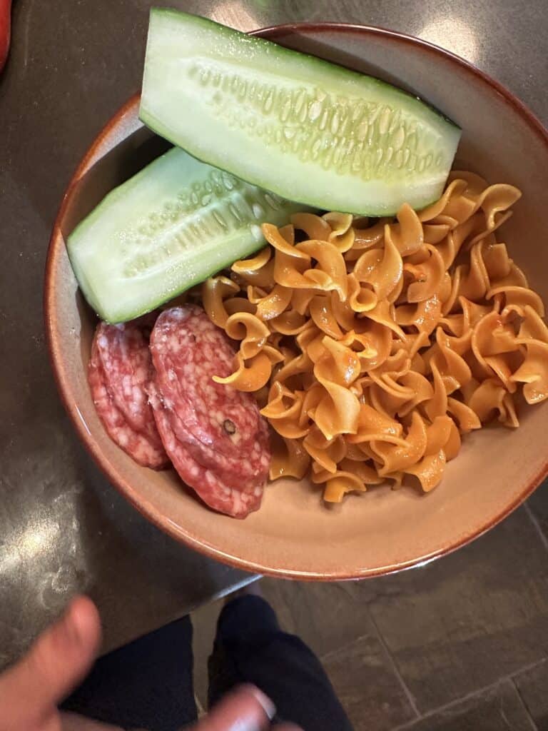 Bowl with chickpea pasta, cucumbers, and sopressata slices. 